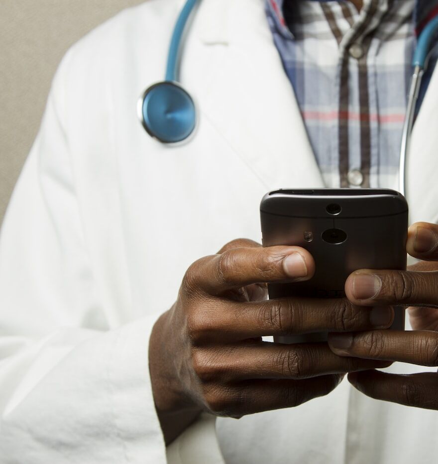 A doctor reviewing patient details on a phone, stethoscope around their neck